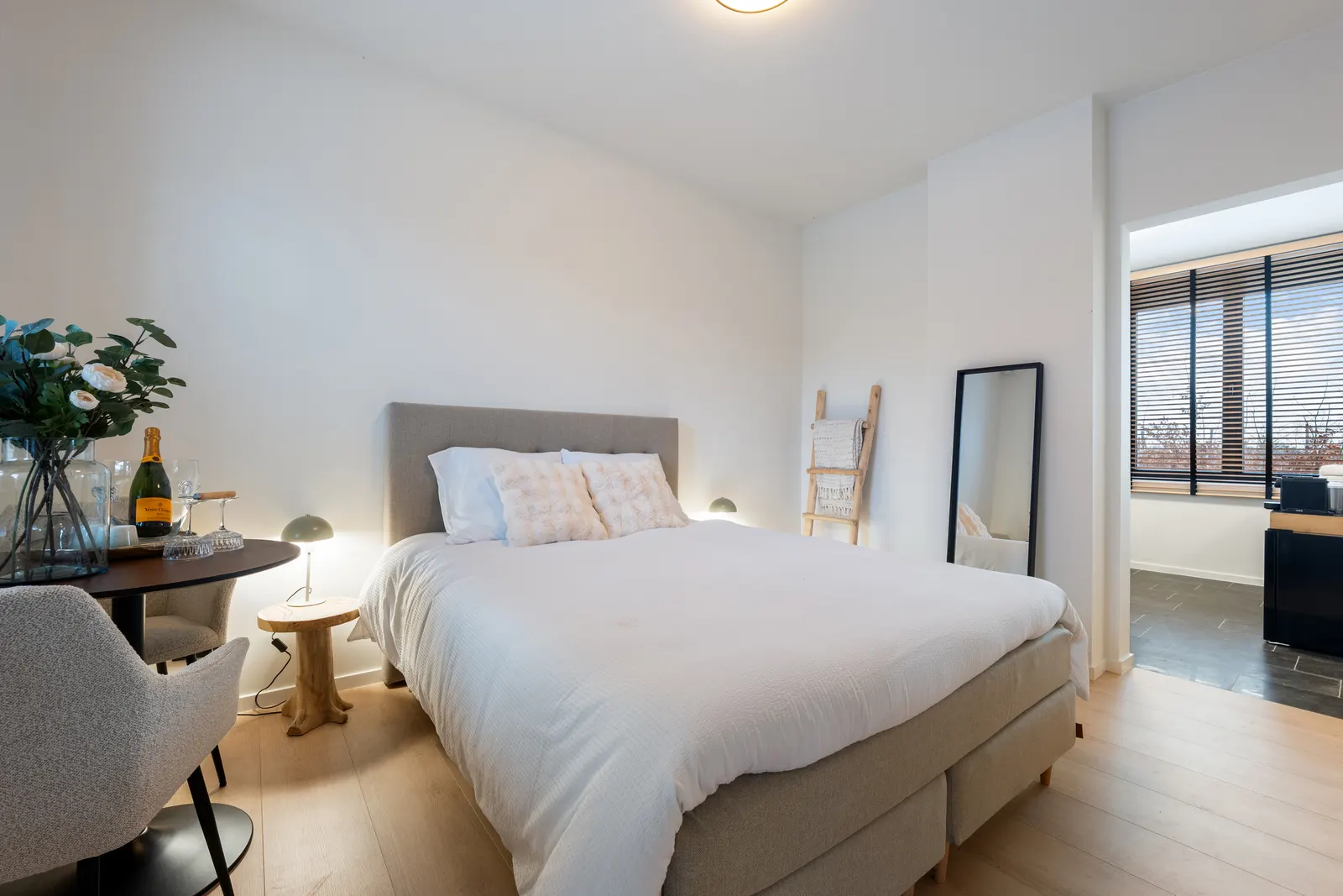 Zwart-witfoto van een slaapkamer met bed, lamp, nachttafel en houten ladder